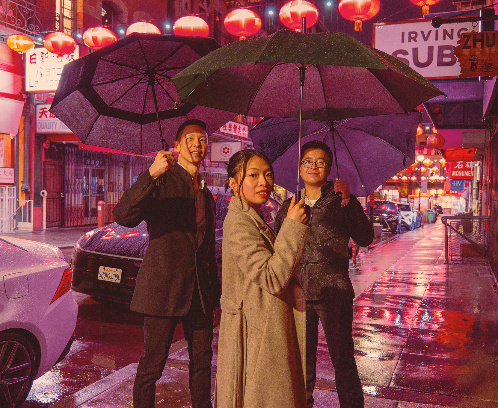 Austin Yu, Wynne Chan, and Derek Ha under umbrellas on a rainy Chinatown street
